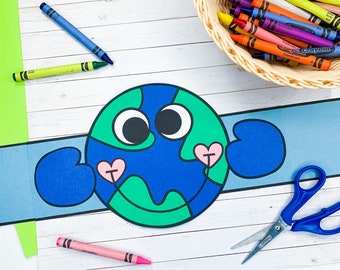 May include: A blue and green Earth craft with googly eyes and pink hearts. The craft is made of paper and has a blue headband. There are crayons, scissors, and a pink crayon on a white wooden surface.