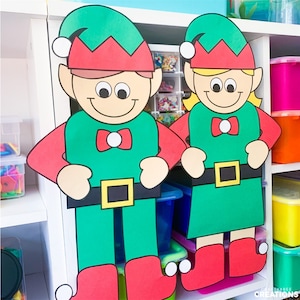Peut inclure: Deux grandes découpes d'elfes en papier, l'une verte et l'autre rouge, avec des pompons blancs sur leurs chaussures. Les lutins sourient et ont de grands yeux. L'elfe vert porte un nœud papillon rouge et une ceinture noire avec une boucle dorée. L'elfe rouge porte un nœud papillon rouge et une ceinture noire avec une boucle dorée.