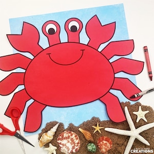May include: Red paper crab craft with a smiling face, on a blue background with brown sand and seashells.
