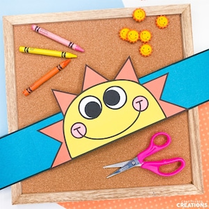 May include: A yellow sun craft with a smiling face, orange rays, and big black eyes. The sun is on a blue and orange headband. There are also crayons, scissors, and yellow smiley face stickers on a corkboard.