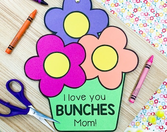 Pode incluir: Um vaso de flores de papel verde com três flores de papel. As flores são rosa, roxo e laranja com centros amarelos. O vaso tem o texto "I love you bunches Mom!" escrito nele.