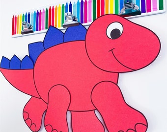 Può includere: Un dinosauro di carta rosso con punte blu sulla schiena. Il dinosauro sorride e ha un occhio grande. Il dinosauro è appeso a una barra bianca con matite colorate.