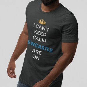 May include: A dark grey t-shirt with a white graphic that says "I can't keep calm, Newcastle are on". The graphic also includes a gold crown.