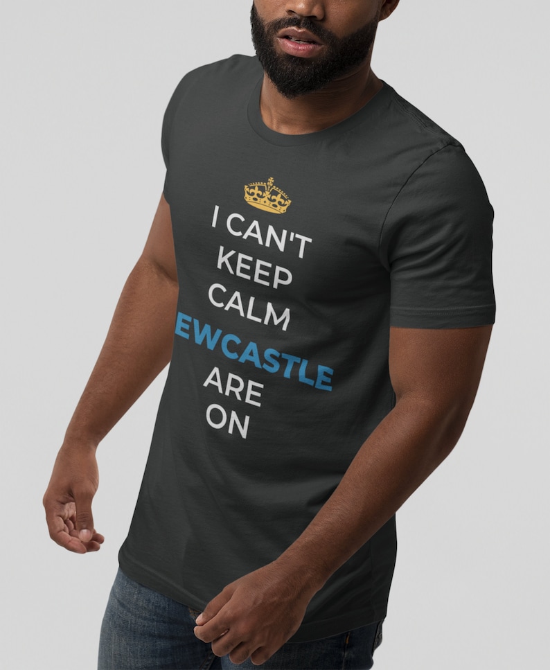May include: A dark grey t-shirt with a white graphic that says "I can't keep calm, Newcastle are on". The graphic also includes a gold crown.