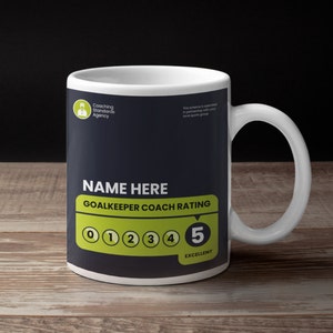 May include: A white ceramic mug with a black and green design. The mug features the text "NAME HERE GOALKEEPER COACH RATING" and a rating scale from 0 to 5, with 5 being "EXCELLENT".