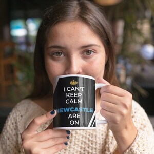 Puede incluir: Taza de cer&aacute;mica blanca con fondo negro y corona dorada. El texto en la taza dice "I can't keep calm Newcastle are on".
