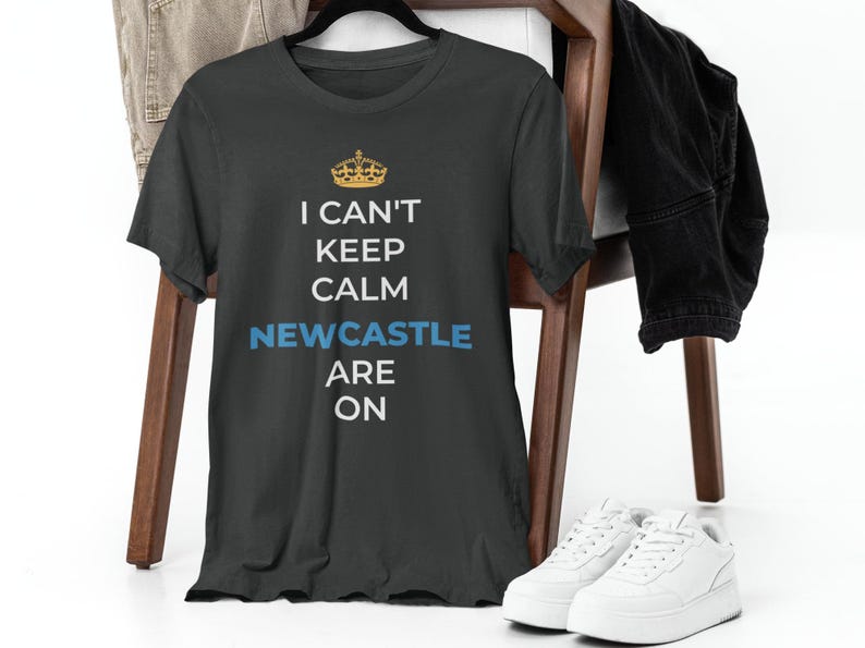 May include: A dark grey t-shirt with a white crown graphic and the text "I can't keep calm Newcastle are on".
