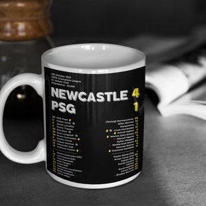 K&ouml;nnte beinhalten: Wei&szlig;er Keramikbecher mit der Aufschrift "NEWCASTLE PSG" und dem Ergebnis 4:1. Der Becher hat einen schwarzen Hintergrund mit gelbem und wei&szlig;em Text und listet Spielernamen auf. Datum und Ort des Spiels sind ebenfalls auf dem Becher aufgedruckt.