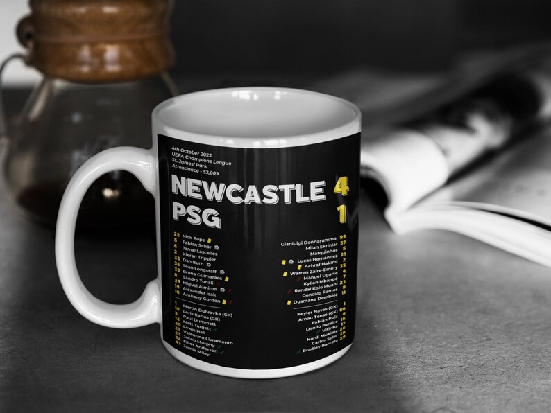 K&ouml;nnte beinhalten: Wei&szlig;er Keramikbecher mit der Aufschrift "NEWCASTLE PSG" und dem Ergebnis 4:1. Der Becher hat einen schwarzen Hintergrund mit gelbem und wei&szlig;em Text und listet Spielernamen auf. Datum und Ort des Spiels sind ebenfalls auf dem Becher aufgedruckt.