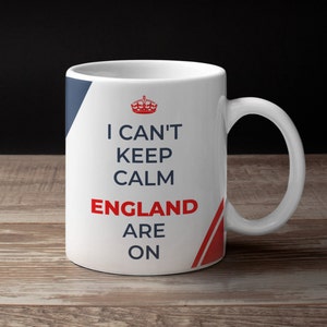 Könnte beinhalten: Eine weiße Keramiktasse mit blauem und rotem Design. Auf der Tasse steht der Text "I can't keep calm England are on".