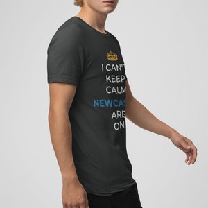 May include: A black t-shirt with a white graphic that says "I can't keep calm Newcastle are on" with a gold crown above the word "can't".