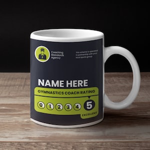 May include: White ceramic mug with a black background and yellow text. The text reads "Coaching Standards Agency", "This scheme is operated in partnership with your local sports group", "NAME HERE", "GYMNASTICS COACH RATING", "0 1 2 3 4 5", and "EXCELLENT".