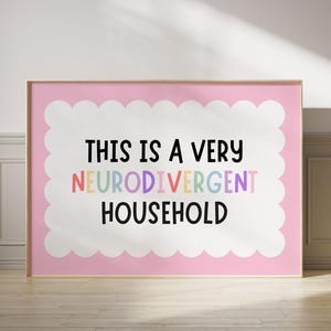 May include: A framed pink print with the text "THIS IS A VERY NEURODIVERGENT HOUSEHOLD" in black and colourful letters. The text is set against a white, scalloped border.
