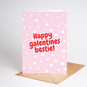 May include: Pink card with white hearts printed on it. The card says "Happy Galentines bestie!" in red letters.