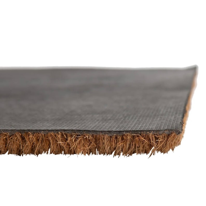 May include: Close-up of a brown coir doormat with a black rubber backing. The mat has a textured surface and is designed to trap dirt and moisture.