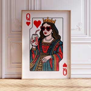 May include: A framed wall art print featuring a playing card design of a queen wearing a gold crown and heart-shaped sunglasses. The figure holds a silver can labeled Diet Coke with a red and white striped straw, set against a white background.