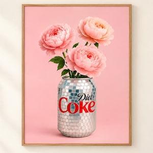 May include: A framed wall art print featuring three light pink peony flowers arranged inside a silver disco ball style soda can. The can displays the red text Diet Coke on its reflective, mirrored surface against a solid light pink background.