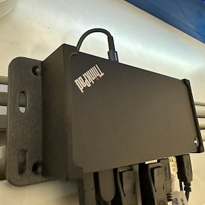 Könnte beinhalten: Eine schwarze ThinkPad Dockingstation mit mehreren Anschlüssen, darunter HDMI, USB und Ethernet. Die Station ist an einer Wand montiert.