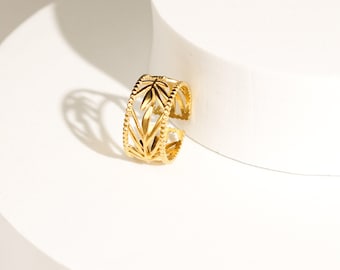 Könnte beinhalten: Ein goldfarbener Ring mit einem durchbrochenen Design und einem sich wiederholenden Blatt- oder Pflanzenmuster. Das Band ist an beiden Rändern mit einer feinen Perlenstruktur versehen, was für ein strukturiertes Aussehen sorgt.