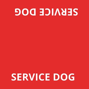 May include: A rectangular red sign featuring the white text SERVICE DOG printed at the top and bottom, with the text DO NOT INTERACT printed vertically along both the left and right sides. A small logo is visible in the bottom right corner.
