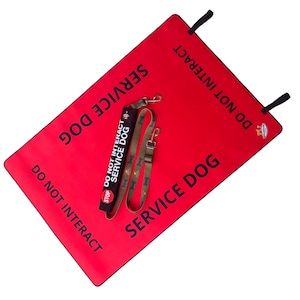 May include: A rectangular red mat with black text reading SERVICE DOG and DO NOT INTERACT, featuring black corner tabs. Included is a black leash wrap with the text DO NOT INTERACT SERVICE DOG and a stop sign icon, plus a tan leash with bone patterns.