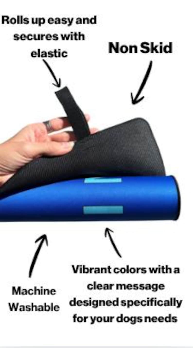 May include: A blue mat with light blue rectangular accents that rolls up and secures with a black elastic strap. The underside is black and non-skid. Text on the image includes: Rolls up easy and secures with elastic, Non Skid, Machine Washable, and Vibrant colors with a clear message designed specifically for your dogs needs.