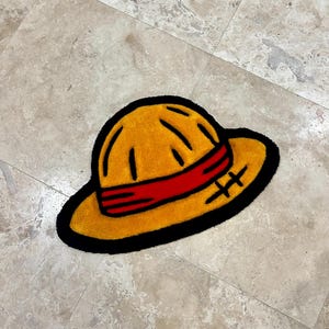May include: A yellow straw hat with a red band and black stitching. The hat is on a light brown tiled floor.