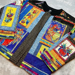 May include: A black t-shirt with a patchwork design. The patchwork features various colorful patterns, including geometric shapes, floral motifs, and stylized figures. The colors include blue, yellow, red, and green.