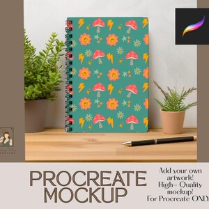 May include: A spiral-bound notebook with a teal cover featuring a repeating pattern of smiling flowers, red mushrooms, and yellow lightning bolts. A black pen rests on the wooden surface next to the notebook. The text "PROCREATE MOCKUP" is at the bottom.