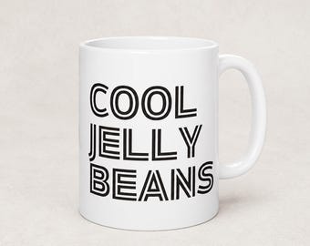 May include: A white ceramic mug featuring the black text COOL JELLY BEANS printed in a bold, double-lined sans-serif font. The mug has a smooth, glossy finish, a cylindrical body, and a curved handle on the right side for holding the beverage container.