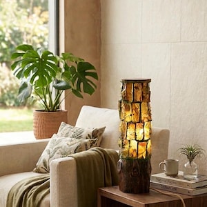 Peut inclure: Une lampe de table cylindrique dotée d'une base et d'un sommet à la texture de bois brun foncé, avec une section centrale composée de panneaux de verre ambré translucide et froissé disposés en grille, diffusant une lueur chaude.