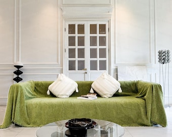 May include: A green sofa with white throw pillows and a glass coffee table in a white room with a white door.