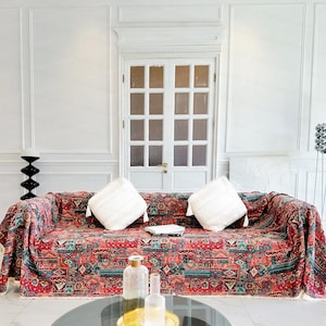 Peut inclure: Une couverture de canapé à motifs rouge, bleu et vert drapé sur un canapé avec des coussins blancs. Le canapé est dans une pièce aux murs blancs et une porte blanche avec des panneaux en verre.