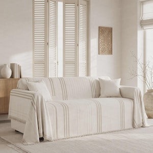 May include: A cream-colored sofa cover featuring vertical beige stripes and a fringed edge. The fabric is draped over a sofa, accompanied by two matching square throw pillows. The text EmbraceComfort is visible at the bottom center.