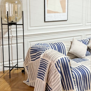 May include: A blue and gray striped throw blanket draped over a couch with a white pillow. The blanket has a geometric pattern of horizontal stripes.