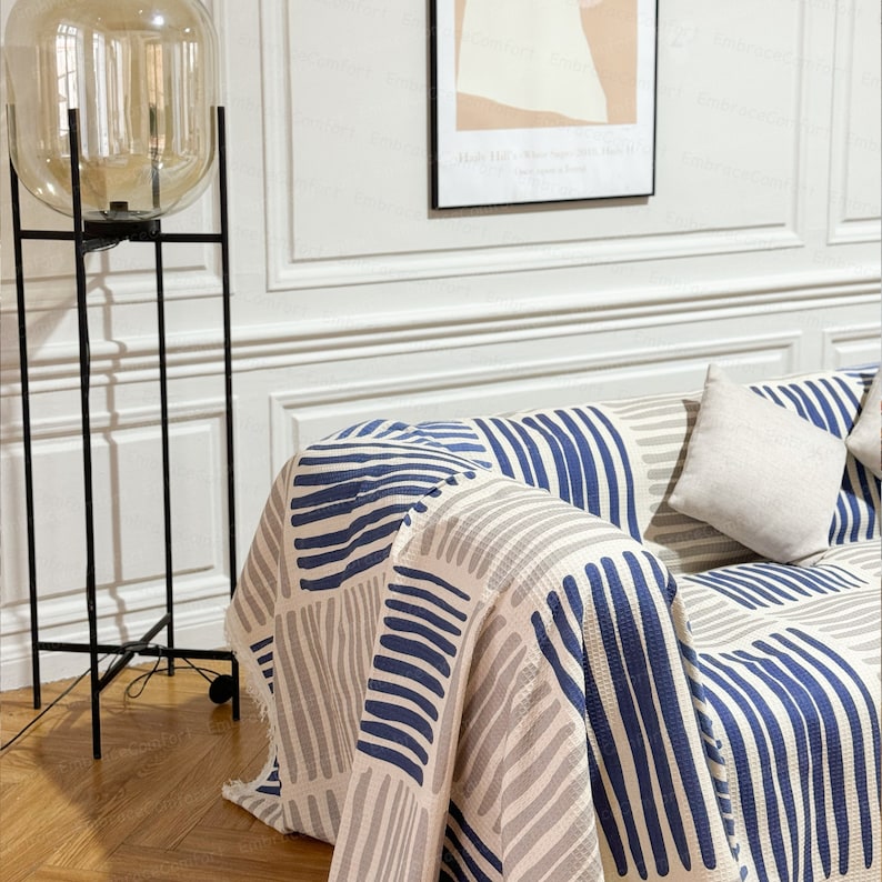May include: A blue and gray striped throw blanket draped over a couch with a white pillow. The blanket has a geometric pattern of horizontal stripes.