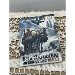 May include: A DVD case for the movie "Van Helsing" featuring a dark, action-packed design. The cover shows two people with a crossbow, a bat, and a castle. The text "Own The Action on DVD & Video Oct. 19" is also visible.