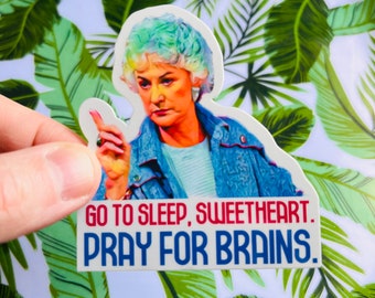 Op de afbeelding: Een sticker met een vrouw met blauw haar en een blauw denim jack. De sticker heeft de tekst "Go to sleep, sweetheart. Pray for brains."
