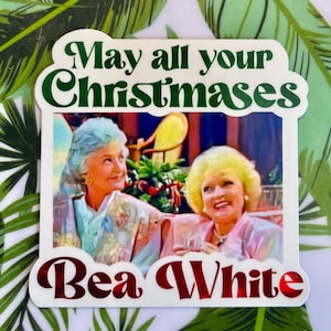 May include: A white sticker with the text "May all your Christmases" in green script above an image of two women. Below the image, the text "Bea White" is in red script. The sticker has a white border and is on a background with green and white tropical leaves.