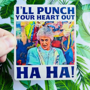 May include: A white sticker with a blue border featuring a photo of a woman with a surprised expression. The text "I'LL PUNCH YOUR HEART OUT HA HA!" is printed in blue letters.