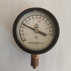 Può includere: Un manometro per la pressione dell'acqua bianco e nero con un ago nero che punta a 90 PSI. Il manometro ha un logo a corona e il testo "WATER PRESSURE EE-12-00".