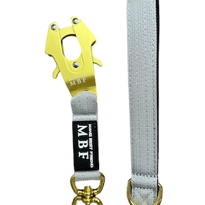 Puede incluir: Una correa gris para perros con un cierre y herrajes de metal dorado. El cierre está grabado con "MBF". La correa tiene una etiqueta negra con el texto "MAN'S BEST FRIEND".