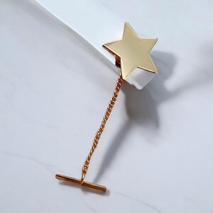 May include: A gold star-shaped tie tack with a chain and a t-bar clasp.