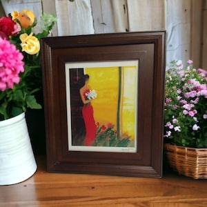 May include: A framed artwork featuring a woman in a red dress holding white flowers, set against a yellow background. The artwork is in a dark brown wooden frame. The image is surrounded by flowers in pots and baskets.