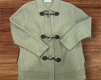 May include: A light green toggle coat with a collared neckline and long sleeves. The coat features three dark brown leather and silver toggle closures down the front. The coat is made of a textured knit fabric.