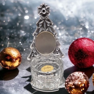 Pode incluir: Um enfeite de árvore de Natal de vidro transparente com um espelho redondo no centro. O enfeite está sentado em uma base de vidro transparente com as palavras "Gotham Germany" em um rótulo.