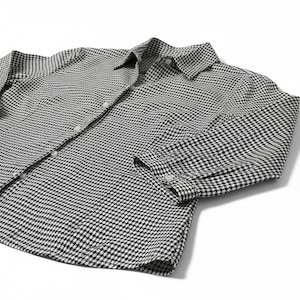 May include: A long-sleeve button-down shirt featuring a small black and white houndstooth pattern. The shirt includes a standard collar, a front button placket with light-colored buttons, and buttoned cuffs on the sleeves, presented in a flat view.