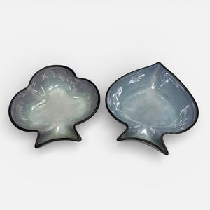 May include: Two decorative glass dishes, one shaped like a club and the other like a spade. The dishes have a pearlescent finish with a black trim. The club dish is on the left, and the spade dish is on the right.