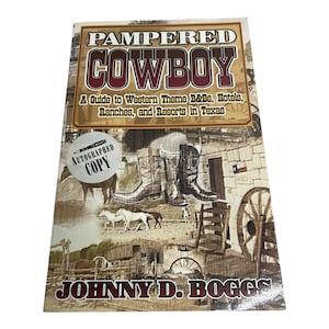 Puede incluir: Un libro titulado "Pampered Cowboy" con el subtítulo "A Guide to Western Theme B&Bs, Hotels, Ranches, and Resorts in Texas". La portada presenta botas de vaquero, caballos y una rueda de carro. Una pegatina de "Autographed Copy" es visible.