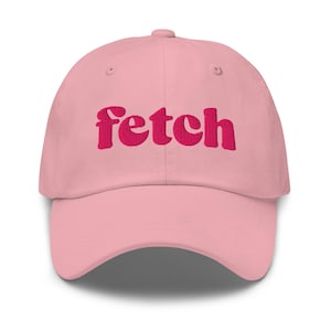Puede incluir: Gorra de béisbol rosa claro con la palabra "Fetch" bordada en rosa oscuro en la parte delantera. La gorra tiene una visera curva y un botón en la parte superior. Un accesorio casual.